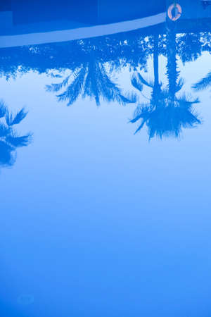 Reflection of palm trees in the water of the swimming pool. Swimming pool with crystal blue water with palm tree reflection as summer holiday and tropical paradise vacation at poolside background. summer timeの写真素材