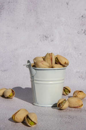 Pistachios in white bucket on concrete background. Healthy and dietary nutrition. Concept of nuts. Vegan protein omega vitamin food. Roasted salty pistachio. Harvestの写真素材