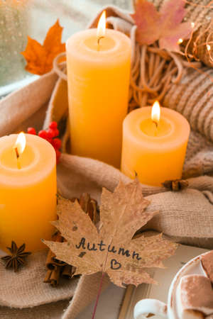 Fall maple leaf with text AUTUMN on Autumn season design concept. Candles on windowsill rainy...