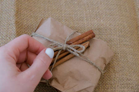 Woman making Box with New Year's gifts, wrapped in craft paper and decorated with cinnamon sticks....