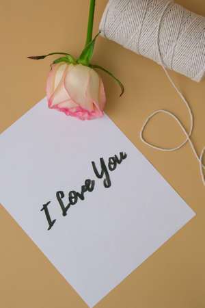 I LOVE YOU text on paper note. Delicate pink roses with spool of white cotton rope on beige...