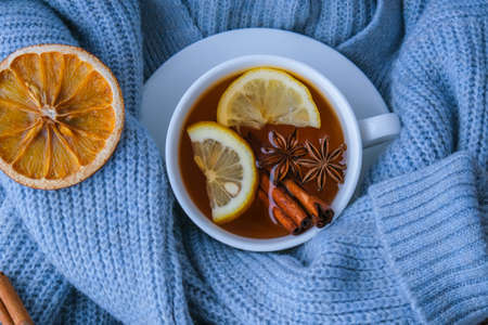 Blue sweater and cup of hot tea with lemon cinnamon sticks and anise star. Dry slices of citrus orange and cones. Hot winter cocktail. Christmas, Thanksgiving drinks. Autumn, grog, hot sangria, mulled wine. Festive holiday flat lay atmosphereの写真素材