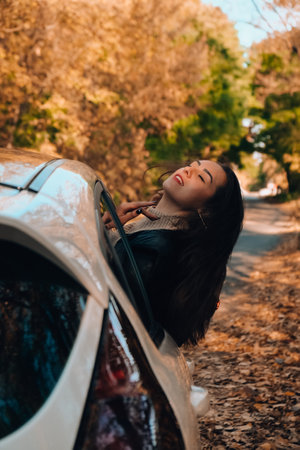 Brunette European looking cute girl sitting in a car enjoying sunny autumn weekend. Travel and road trip. Woman looking at the view from a car. Happy woman enjoying road tripの写真素材