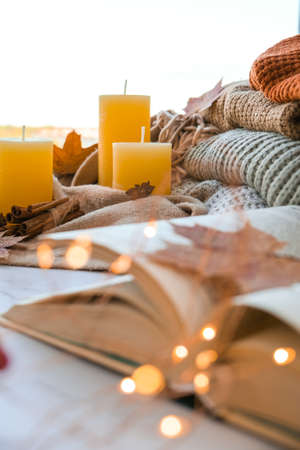 Book on first plan Thanksgiving and Hello Fall, celebrating autumn holidays at cozy home on the windowsill Hygge atmosphere Autumn leaves, spices and candle on cozy knitted sweater in warm yellow lights. selective focusの写真素材