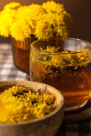 Dandelion flower healthy tea in glass cup on table. Herbal medicine Delicious tisane tea from with fresh yellow blossom dandelion flowers inside tea cup. Green clearing infusion Wildflowers Eco friendly organic brand concept. Nice greeting card for International tea day Herbal beverageの写真素材
