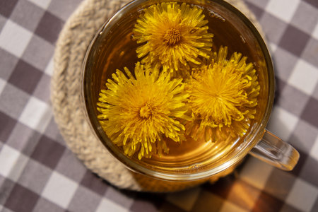 Dandelion flower healthy tea in glass cup on table. Herbal medicine Delicious tisane tea from with fresh yellow blossom dandelion flowers inside tea cup. Green clearing infusion Wildflowers Eco friendly organic brand concept. Nice greeting card for International tea day Herbal beverageの写真素材