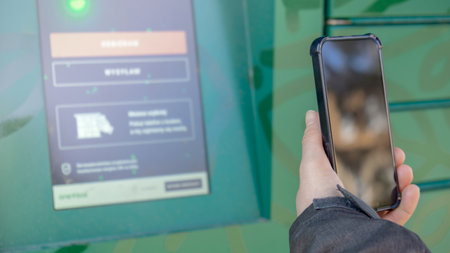 Female hand holding mobile phone next to Parcel locker Collecting parcel from shopping locker. Woman Skans QR Code on Mobile phone Self-service Locker Cell with Bar code Reader Modern Shipping and Delivery Concept with Contactless Automated Postal Boxの写真素材