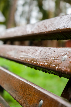 Wet bench in the park in the rain. rainy weather. Wooden chair in the rain. Wet urban furniture. Raindrops on wooden bench. park autumn conceptの写真素材