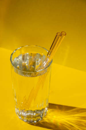 Reusable glass Straws in Glass with water on yellow background Eco-Friendly Drinking Straw Set with cleaning brush. Zero waste, plastic free concept. sustainable lifestyle. Waste free living Low wasteの写真素材