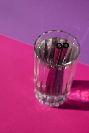 Reusable glass Straws in Glass with water on purple violet background Eco-Friendly Drinking Straw Set with cleaning brush. Zero waste, plastic free concept. sustainable lifestyle. Waste free living Low wasteの写真素材