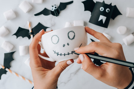 Female hands paint on white cup scary jacks face DIY for kids Halloween home activities Holiday art children craft Handmade decorations. Step by step Socially distanced at home Idea for art classの写真素材