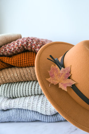 Stack of cozy knitted warm sweater with Autumn fall maple leaf and beige stylish hat. Sweaters in retro Style. orange and blue colors. Cozy hygge concept Copy space Autumn seasonの写真素材