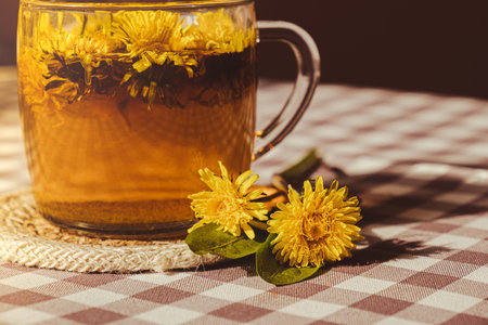 Dandelion flower healthy tea in glass cup on table. Herbal medicine Delicious tisane tea from with fresh yellow blossom dandelion flowers inside tea cup. Green clearing infusion Wildflowers Eco friendly organic brand concept. Nice greeting card for International tea day Herbal beverageの写真素材