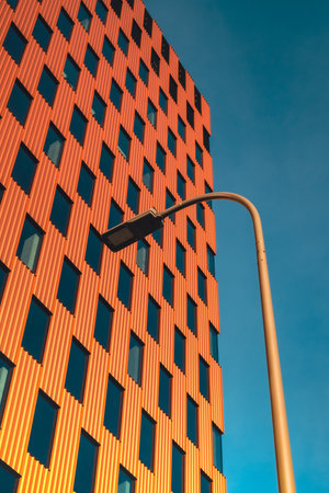 Modern office building exterior with glass facade on clear sky background. Transparent glass wall of office building with orange decoration with lantern. Creative Photo Element of facade of modern European building Commercial office buildings. Abstract modern business architectureの写真素材