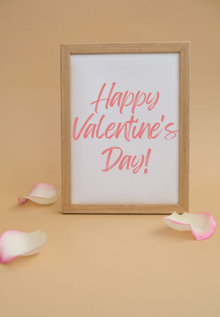 Wooden frame with text HAPPY VALENTINES DAY on paper blank and delicate pink rose petals on beige background. Romantic pastel pink rose flowers. Neutral earth tones. Greeting card holidayの写真素材
