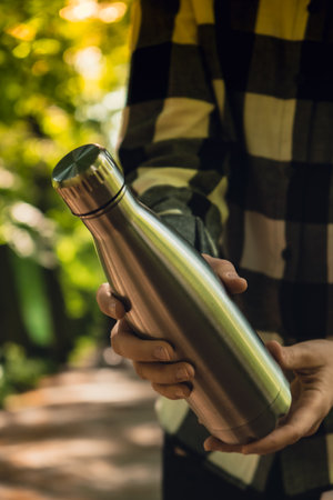 Close-up of Unrecognizable female hand holding Water bottle. Reusable steel thermo water bottle in park. Sustainable lifestyle. Plastic free zero waste free living. Go green Environment protection. Woman drinking water in parkの写真素材