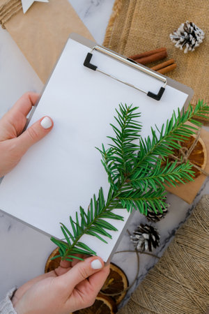 woman preparing for christmas holidays. Writing gift list. Box with New Year's gifts, wrapped in craft paper and decorated with fir branch, dry orange slices, cinnamon sticks. Handmade Eco friendly alternative green Christmas presents zero waste Sustainable lifestyleの写真素材