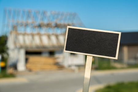 Blank Black billboard against House is in the process of being renovated. Empty mockup template Blackboard label Construction of house. Copy space Unfinished building. Renovation work. Private house wit wooden roof Development of real estate in modern city suburbsの写真素材