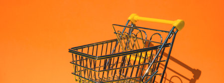Empty shopping trolley cart on colorful orange yellow background. Copy space for your text. Online shopping, buy mall market shop consumer concept. Small toy supermarket grocery push cart. food crisis. Rising food cost, food prices shortage mass hunger. inflationの写真素材