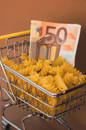 Shopping trolley cart Filled With Pasta with 50 euro paper money banknote on Beige background. Copy space for your text. Food and groceries shopping price increase, Rising food cost food crisis inflation concept. Online shopping, buy mall market shop consumerの写真素材