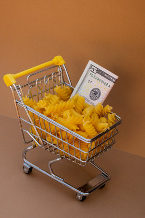 Shopping trolley cart Filled With Pasta with 5 US dollar paper money banknote on Beige background. Copy space for your text. Food and groceries shopping price increase, Rising food cost food crisis inflation concept. Online shopping, buy mall market shop consumerの写真素材
