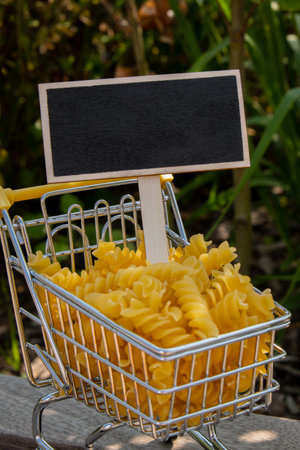 Empty mockup template Blackboard label against Shopping trolley cart Filled With Pasta on agriculture background. Copy space for your text. Food and groceries shopping price increase, Rising food cost food crisis inflation concept. Online shopping, buy mall market shop consumerの写真素材