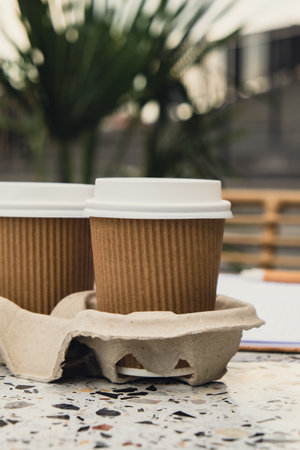 Two paper cups with lid for tea to go. Coffee take away on the table. Take-out coffees with brown paper cup holder. Brown safety cardboard collars. Cardboard trayの写真素材