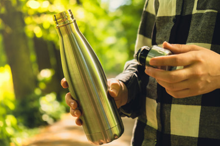 Close-up of Unrecognizable female hand holding Water bottle. Reusable steel thermo water bottle in...