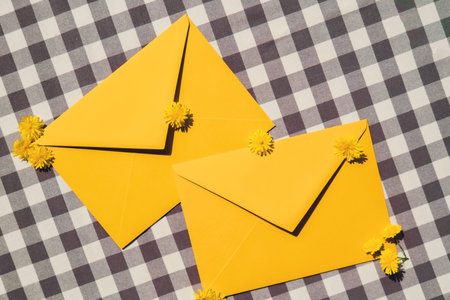 Beautiful little yellow chamomile daisies flowers on two postal yellow envelopes, empty paper note copy space for text, spring time, greeting card for holiday. Flower deliveryの写真素材
