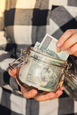 Polish zloty banknote saving money in glass jar. Unrecognizable woman moderate consumption and...