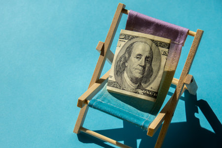 Rolled Up Hundred Dollar Banknote On Miniature Deck Beach Chair. Concept of costs in travel holidays. Save for vacation. copyspace. The concept of how much it costs to restの写真素材