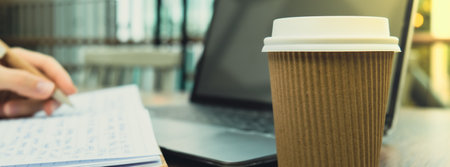 Unrecognizable Young woman study at wooden table in shopping mall food court. Drinking coffee from paper cup. Student making homework Female hands writing on notebook gratitude journal self reflection self discovery in Co-Working Space. Goals, to-do list in the modern office buildingの写真素材