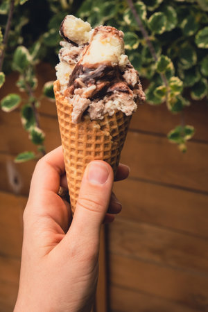 Female hand holding delicious american vanilla chocolate ice cream. Tasty homemade icecream Gelato in the waffle cone. Gluten free vegan dairy freeの写真素材