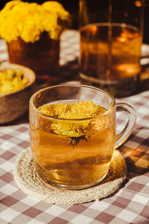 Dandelion flower healthy tea in glass teapot and glass cup on table. Delicious herbal Hot tea from fresh dandelion flowers at home at summer day. Green clearing. Bouquet of dandelions petalsの写真素材