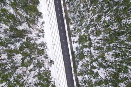Aerial view on road in winter time, road surrounded with forest trees. Rural winter area. Top view landscape. shooting from drone. Snow covered road in winter forestの写真素材