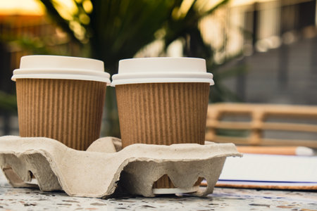 Two paper cups with lid for tea to go. Coffee take away on the table. Take-out coffees with brown paper cup holder. Brown safety cardboard collars. Cardboard trayの写真素材