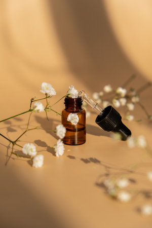 Small bottle of serum on neutral beige background. Beauty pipette dropper with Gypsophila or babys breath white flowers. Glass dropper of cosmetic oil and dried flowers and herbs. Natural organic herbal skin care oil. Facial liquid serum with collagen and peptides. Monochrome conceptの写真素材