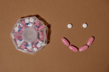 Organizer weekly shots with smile made of tablets for daily take medicine with white pink drugs and capsules. Daily vitamins at home. Health care and diseases cureの写真素材
