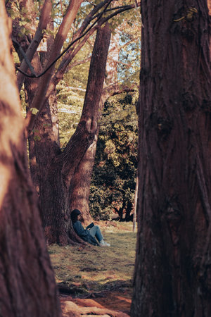 Attractive young woman reading book while sitting on grass in green public park. Springtime outdoors. Greenery unity with nature. Spend free time on open airの写真素材