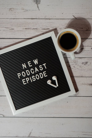 Announcement Letter board with text NEW PODCAST EPISODE on wooden table with white cup of coffee wireless headphones. Podcasting concept. Listening radio audio healing wellness soundの写真素材