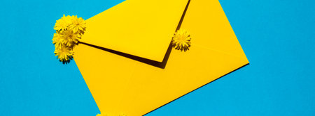 Beautiful little yellow chamomile daisies flowers on postal yellow envelope on blue background, empty paper note copy space for text, spring time, greeting card for holiday. Flower deliveryの写真素材