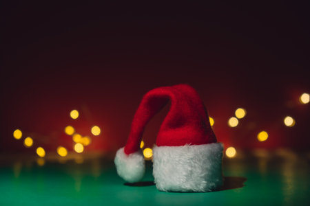 Santa hat on isometric green red background. Defocused lights on backdrop Copy space for your text. Mock up for advertisement. Holiday Christmas composition. Minimalistic greeting cardの写真素材