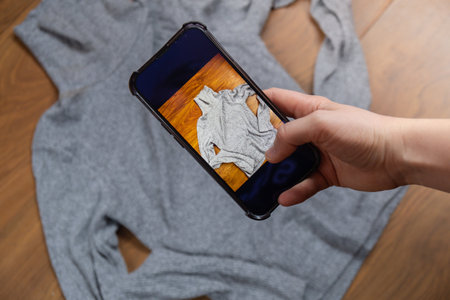 Woman taking photo of clothing to sell online. Second hand sustainable shopping Concept of selling clothes online. Sustainable fashion overconsumption, conscious buying consumption, slow fashion clothes with phone app and doing e-commerceの写真素材