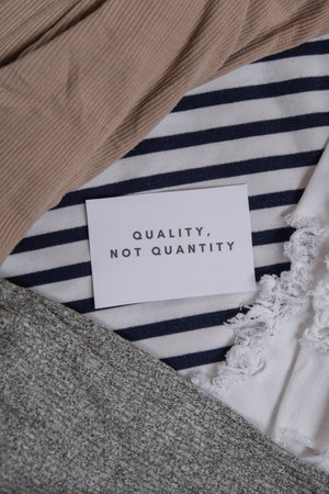 Quality not quantity text on paper note on clothes assortment Second hand sustainable shopping. Capsule minimal wardrobe. Sustainable fashion overconsumption, conscious buying consumption, slow fashionの写真素材