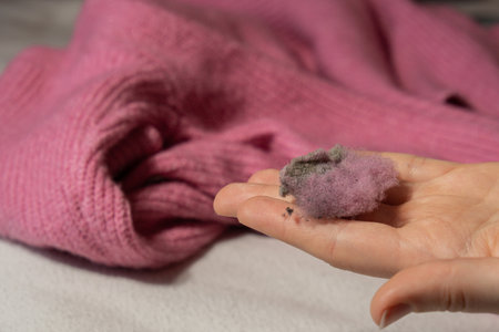 Woman using Anti-pilling razor at home. Device for shaving clothes. Anti-Plush fabric Shaver. Electric portable sweater pill defuzzer Lint remover from pink acrylic or wool sweater. Slow fashion mending repairingの写真素材