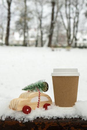 Wooden car carrying Christmas tree with paper cup mock up of coffee or hot chocolate over snow. Copy space for text Toy car in snowy landscape. Merry Christmas and Happy New Year conceptの写真素材
