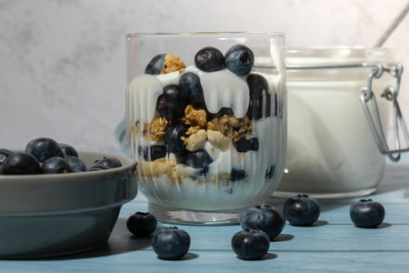 Morning granola breakfast with homemade greek yogurt, blueberries in glasses on blue wooden background. Healthy diet Crunchy granola with yogurt nuts and blueberriesの写真素材
