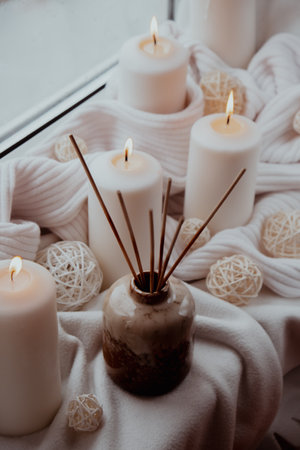 Aroma reed diffuser. Bottle container with wood stick diffusers Essential oils to scent your home fragnance concept autumn holidays at cozy home on the windowsill Hygge aesthetic atmosphere on knitted white sweater. Still life of micro moment candid slow living. Mental health wellbeing exercisesの写真素材