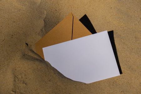 Beige natural tones Envelope with empty white paper note copy space for your text in the sand at the beach. Card mock-up and craft envelope Summer still life scene. Sandy beach background or desert. Tropical vacation conceptの写真素材