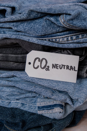 CO2 neutral emission text note on stack of jeans. Ecology nature friendly, climate change, green fuel and earth protect concept. Carbon emission paper recycled label. Natural organic jeans clothing tagの写真素材